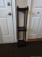 Front view of the 3 tier mahogany wooden plant stand, showing height and design against wall and door context.