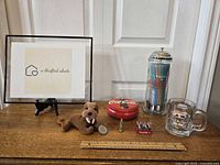 Photo showing Coca Cola and A&W collectibles arranged on a wooden surface including straw dispenser, mug, tin, miniatures and plush toy