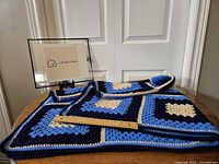 Full view of the handmade crochet blanket folded on a table with a ruler to show size and a small framed sign in the background.