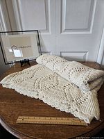 Folded cream crochet blanket displayed on a wooden table with a ruler showing size, highlighting the overall texture and edge design.