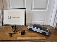 Wide photo showing Kinyo VHS tape rewinder shaped like a car, power cable, and framed wall decor behind.