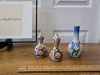 Three small pottery vases on wooden surface in front of white door, showing their shapes and decorative patterns.