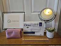 Wide shot of all items: mirror, artificial plant, makeup bag, Dove soap pack and framed photo in background