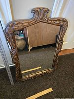 Full front view of the medium-sized antique mirror showing carved wooden frame with leaf and scroll details and clear reflective glass.