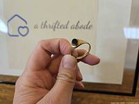 Ring held by hand showing top view of round black stone set in gold bezel