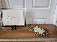 Photo of the whole ornate Syroco mirror showing intricate wood floral design and some surface hazing on the round mirror, placed on a wooden surface with ruler for scale (about 27 inches tall).