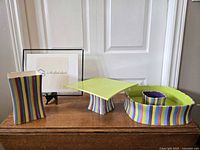 Full view of four ceramic serveware pieces including chip & dip bowl with integrated dip container, candy vase, cake plate with pedestal, and smaller bowl nested in chip & dip bowl. Items show colorful vertical stripes and a waved rim on the large bowl.