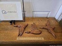 Three pottery geese wall hangings laid flat on wooden surface with ruler for scale.