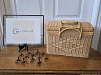 Front view of small wicker picnic basket with 13 black plastic ant-shaped appetizer holders arranged in front of it.