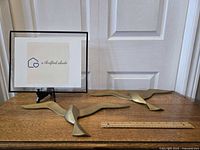 Pair of solid brass seagull wall hangings on wooden table with ruler for size scale, white door background.