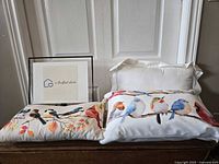 Three decorative pillows arranged against a door; two have colorful bird designs on white background, one is plain cream-colored.