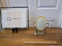 Front view of vintage brass swan swivel vanity mirror next to a ruler for size reference on wooden surface.