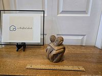 Front view of the handcarved wooden hugging couple sculpture with a ruler for size reference, showing the figures sitting and embracing.