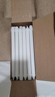 Open box showing multiple white taper candles neatly packed inside the carton.