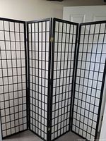 Full view of the four-panel privacy screen standing unfolded, showing black framing and white grid panels.