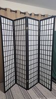 Front view of four-panel privacy screen room divider with black wooden frame and white paper inserts in grid pattern, set on carpet.