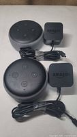 Top view of two Amazon Echo Dot 3rd generation smart speakers, each with power adapter coiled beside it, showing button layout and fabric covering.