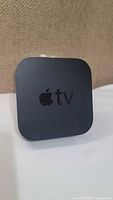 Front view of the Apple TV streaming device showing Apple logo and 'tv' lettering on top surface.