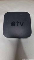 Top view of black Apple TV device with Apple logo and 'tv' text, showing some scratches and wear.