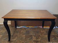Wooden kitchen table without expansion leaf attached, showing natural wood top and curved black legs, photographed from the side.