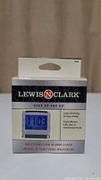 Front side of the retail box for the Lewis and Clark portable alarm clock showing the product image, brand name, and description with large LED display.