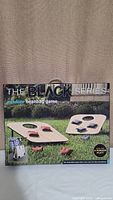 Box front showing title The Black Series outdoor beanbag game for 4 players with image of game setup in grass.
