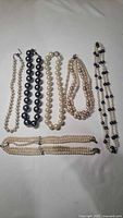 Lot of six costume jewelry pearl necklaces displayed on white fabric, showing variety in bead sizes and colors.