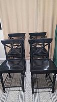 Set of 4 black wood high-top bar chairs with cross-back design shown from the front facing the camera.