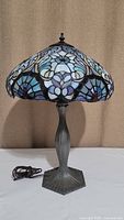 Full front view of Tiffany style lamp with decorative plastic shade and metal base. Corded power visible on left.