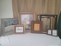 Various framed artworks grouped on a white table against a beige curtain, showing entire collection