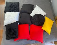 Photo showing 10 decorative accent pillows in black, white, red, and yellow with various textures and designs arranged on bed.