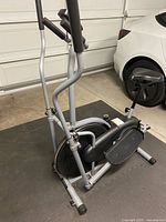 Side angle view showing heavy-duty steel frame, flywheel, pedals, and dual handlebars of elliptical machine