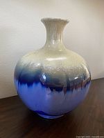 Image of a round ceramic floor vase with a narrow neck, glazed in cream fading into blue color.