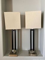 Photo showing a pair of modern nightstand table lamps with beige rectangular shades and black metal bases inside a recessed niche.