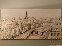 Photo of rectangular canvas painting showing Paris cityscape with Eiffel Tower and a river with bridges in sepia tones
