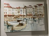 Frontal view of the painting showing boats on a canal with buildings behind them, hung on a wall.