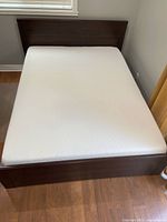 Full view of dark brown bed frame with white mattress against wall under window