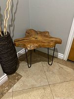 Side table positioned in a corner with a natural curved wood slab top and black metal hairpin legs, showing the table's profile and base