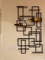 Front view of geometric black metal wine rack mounted on a wall holding two wine bottles horizontally.
