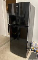 Front view of Whirlpool black top freezer refrigerator showing both doors closed and glossy finish.