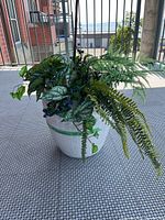 White ceramic pot filled with artificial greenery and berries on grey textured surface outside.