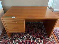 Full view of teak desk showing wooden surface, two drawers on left and legs on the floor rug.