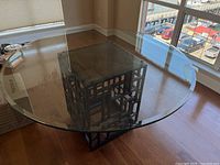 Round glass top dining table with geometric metal base, showing full view of the table and its design.