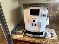 Front view showing white Jura machine on countertop with filter cartridge box at left and two cleaning tablet boxes at right
