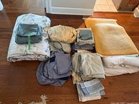 Full lot display of linens and small rug spread on wood floor showing various linens and yellow area rug.