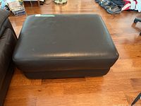 Top view of the brown leather ottoman on wood flooring.