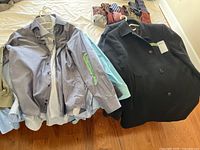 Several men's dress shirts stacked on hangers with visible size tags, variety of colors and patterns including stripes and solids.