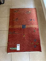Full view of the small reddish-brown rectangular area rug with colorful small motifs and white fringe edges, placed on a tile floor.