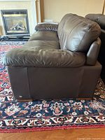 Side profile of brown leather sofa on patterned rug with fireplace in background