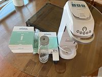 White Sparkel beverage carbonation machine with accessories including carbonating bottle, replacement carbonators, tubing, manual on glass table